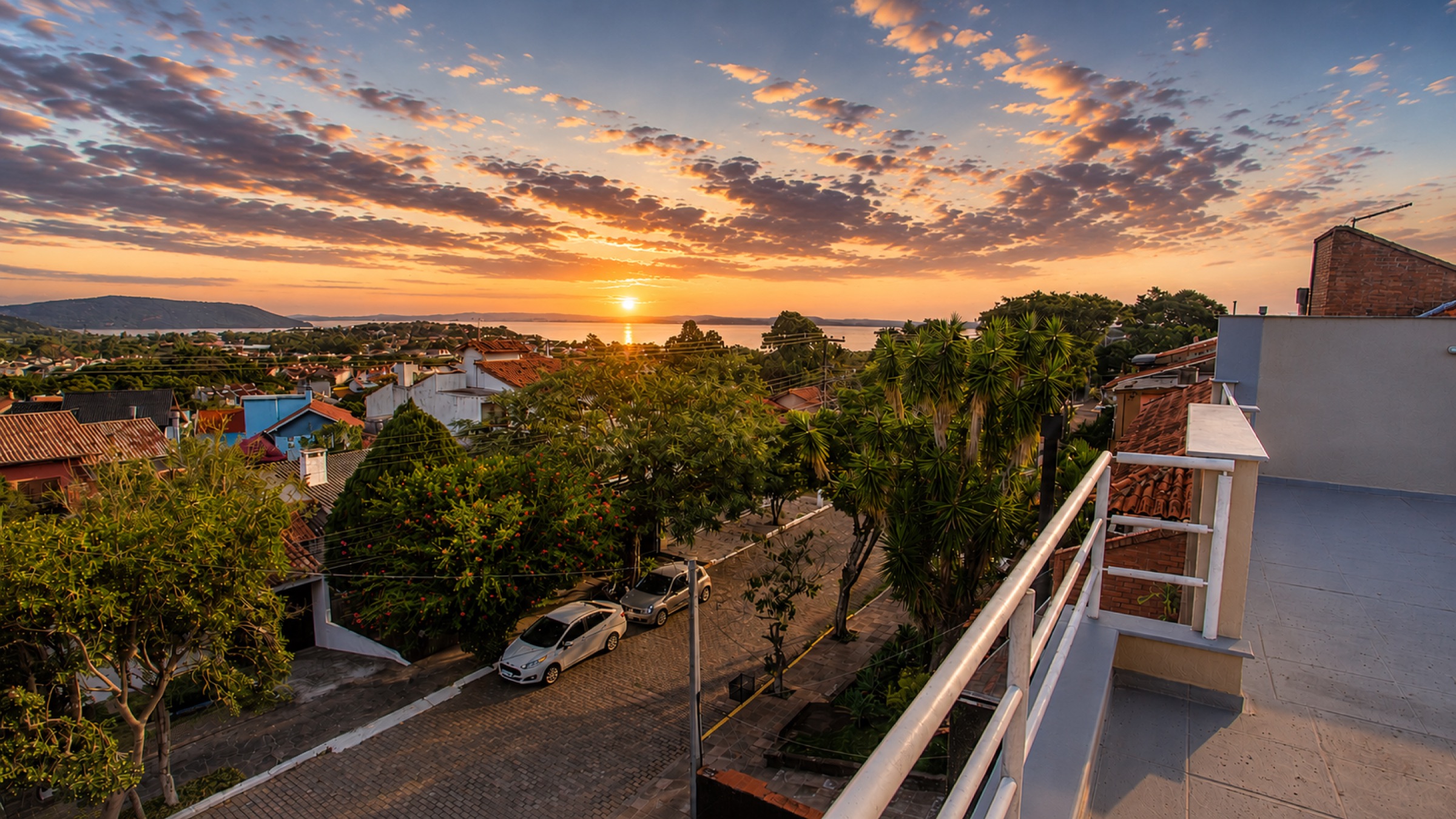 Pôr do sol sobre o Rio Guaíba visto do terraço da casa, com o bairro arborizado em primeiro plano