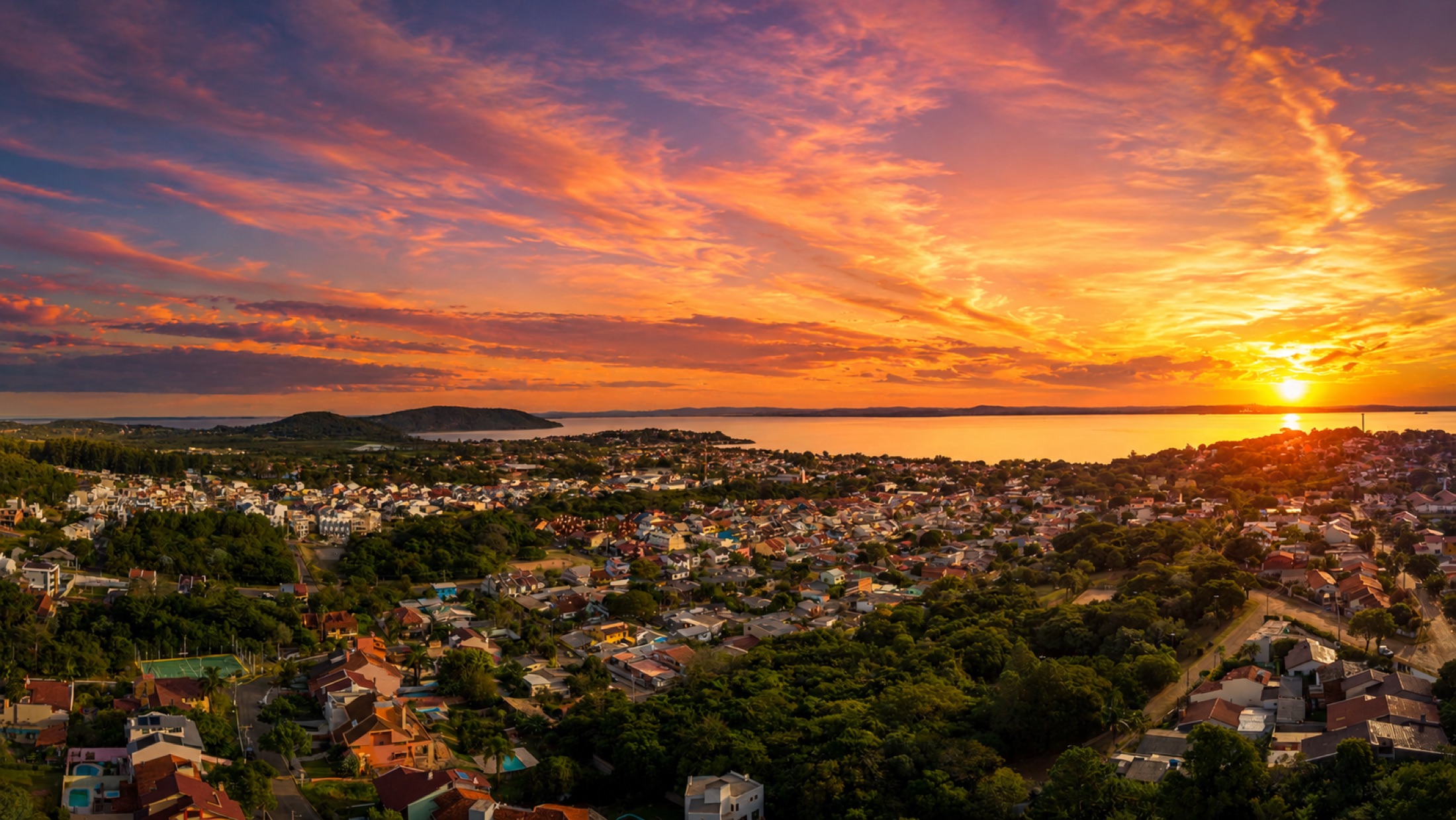 Vista panorâmica aérea da região ao pôr do sol, com o Rio Guaíba ao fundo